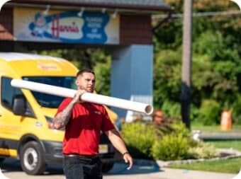 A Harris employee carries a pipe in front of a company building and truck.