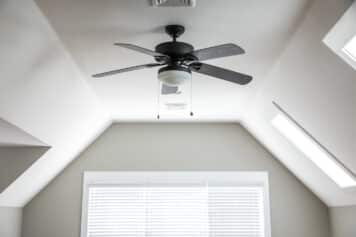 Open and airy bonus room game room in a new construction house with a dark wood ceiling fan, a window and blinds